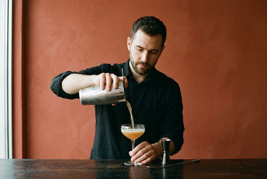 A bartender pouring a cocktail into a coupe glass