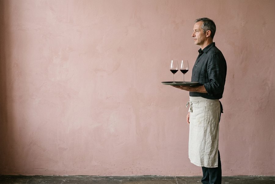 A bistro waiter carrying two glasses of red wine