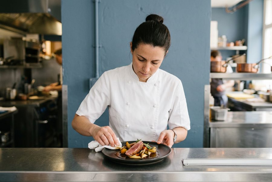 A chef wiping the rim of a plate at the pass